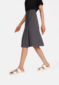 Gonna grigia a pieghe con vita aderente, abbinata a sandali bianchi con due cinturini regolabili e suola spessa.