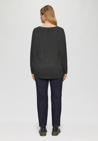 Zwart gespetterd shirt met lange mouwen en een wijde halslijn, gecombineerd met donkerblauwe broek en zwarte enkellaarsjes, gefotografeerd vanachter.
