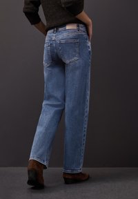 Jasnoniebieskie jeansy z prostą nogawką, z efektem sprania i tylnymi kieszeniami. W zestawie brązowe zamszowe botki za kostkę.