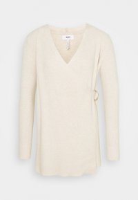 Pull enveloppant en maille côtelée couleur crème avec manches longues et détail de boucle sur le côté, taille petit.