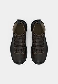 Hnědé kožené turistické boty s černou gumovou podrážkou, vybavené texturovanými tkaničkami a polstrovaným límcem. Minimální šití a poutko na patě.