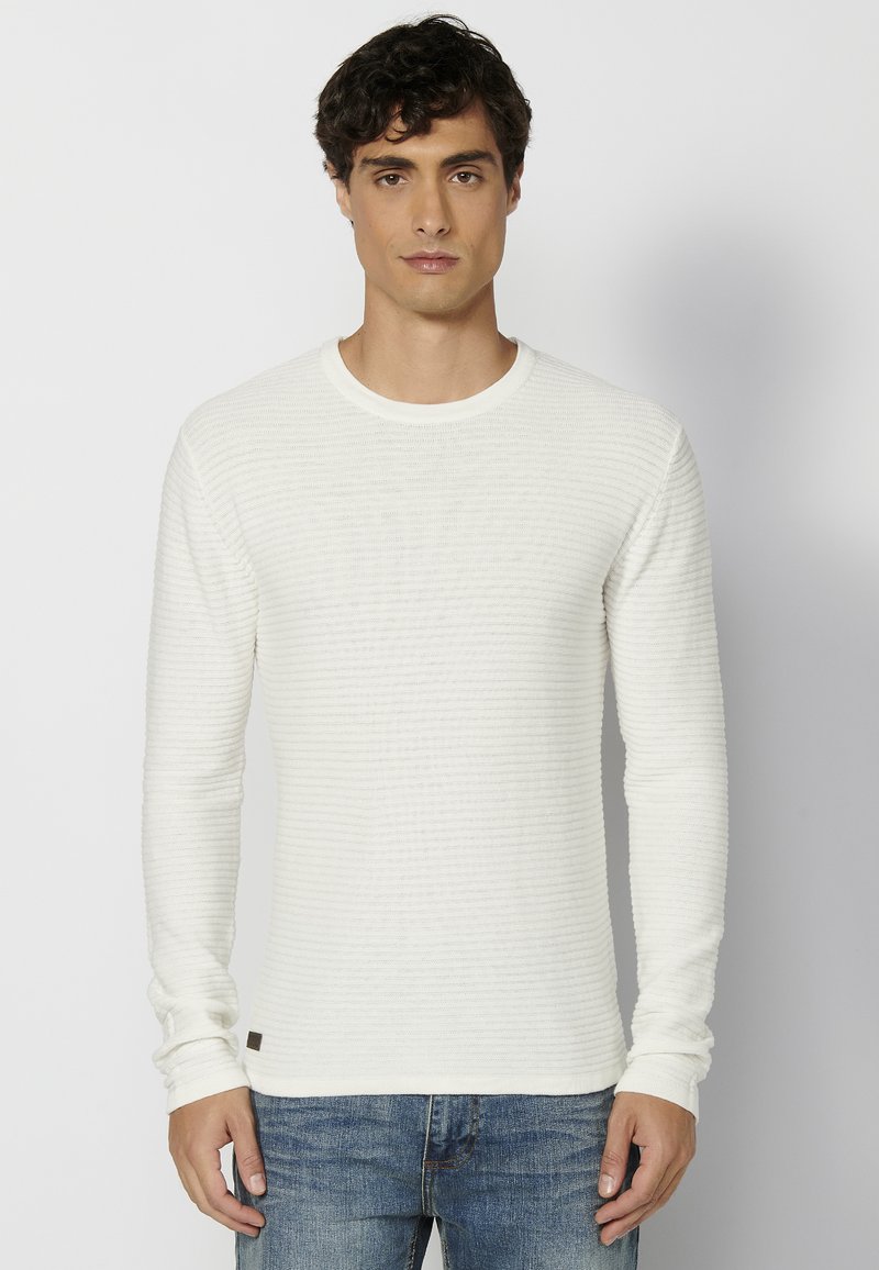Lichtgewicht, geribbelde witte langearmige shirt met een ronde hals en contrasterende stofaccenten aan de zoom. Gecombineerd met blauwe denim jeans.