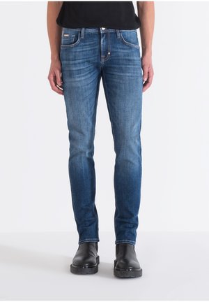 Blue denim jeans with a straight cut, five-pocket design, and subtle whiskering. Worn with black ankle boots, standing against a white background.
