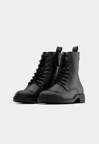 Stivaletti neri in pelle con finitura liscia, punta tonda, lacci anteriori e linguetta sul retro per una facile calzata. Design con suola piatta.