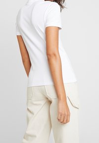 White short-sleeve polo shirt with a fitted design, smooth texture, and a crew neckline, paired with light beige, loose-fitting pants.