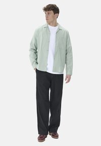Light green button-up shirt with a single chest pocket, worn over a white T-shirt, paired with black pants and brown shoes.