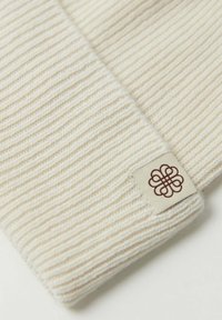 Elfenbensfärgad ribbad scarf i mjukt tyg, med en krämfärgad etikett och en brun logotyp i hörnet. Texturen är framträdande med detaljerade ränder.