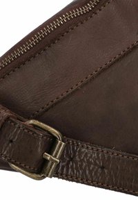 Primo piano di una sezione di una borsa in pelle marrone con una fibbia metallica e il cursore della zip visibile lungo il bordo.