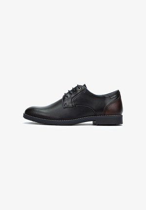 Zapato de vestir de cuero negro con punta redondeada, diseño con cordones, detalle en marrón en el talón y suela texturizada para mayor agarre.