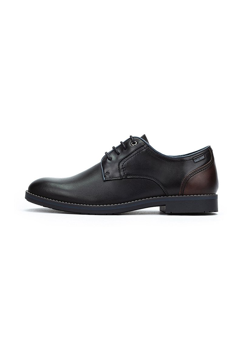 Chaussure de ville noire en cuir avec un bout arrondi, un laçage, un accent marron au talon et une semelle texturée pour une bonne adhérence.