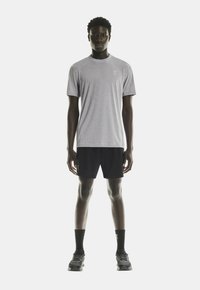 Grå kortærmet atletisk t-shirt med rund hals, parret med sorte shorts. Modellens iført sorte sneakers og sokker.