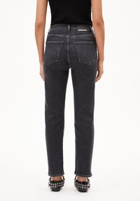 Hoge taille zwarte denim jeans met een rechte pijp, twee achterzakken en een leren merkpatch op de tailleband; gedragen met zwarte hakken.