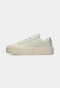Sneaker low-top bianco sporco con suola piatta spessa, design con lacci e dettagli di cucitura minimi, mostrato in profilo laterale su uno sfondo neutro.