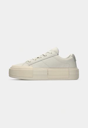 Baskets basses off-white avec une épaisse semelle plateforme, design à lacets et détails de couture minimalistes, présentées en profil latéral sur un fond uni.