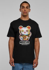 Sort bomulds T-shirt med et farverigt grafisk design af en bjørnefigur med poter, teksten "WELCOME" og "GOOD FORTUNE" nedenunder. Korte ærmer og afslappet pasform.