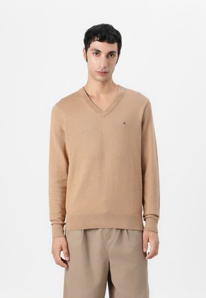 Beige V-neck sweater made of soft fabric, featuring long sleeves and a ribbed hem. Small logo detail on the chest.
