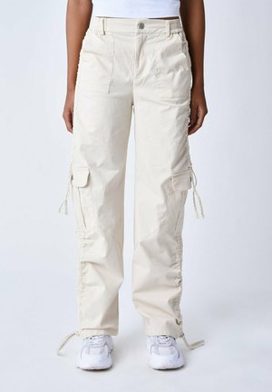 Pantalones cargo de color beige claro con tejido texturizado, que cuentan con cordones ajustables a los lados, bolsillos frontales y un corte relajado.