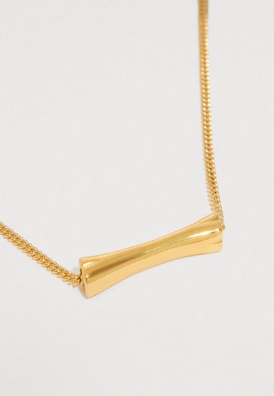 Colar dourado com um pendente cilíndrico liso e afilado numa corrente fina, sobre um fundo claro.