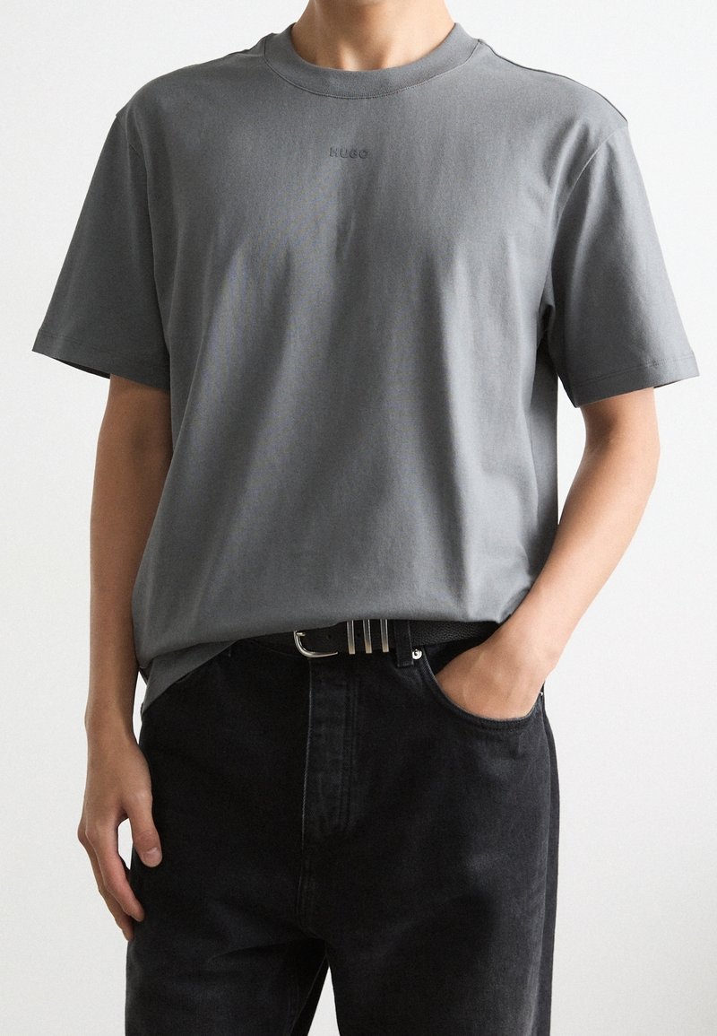 Grijze korte mouwen t-shirt met een ronde hals en subtiele branding. Gekocht met zwarte jeans met een riem met een zilveren gesp.