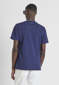 Navy blue cotton t-shirt with short sleeves, crew neckline, and subtle logo detail on the back. Smooth texture, casual design.