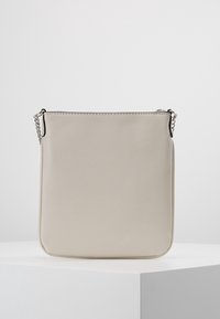 Bolso rectangular cruzado beige con superficie texturizada y correa de cadena plateada, de pie sobre un pedestal blanco contra un fondo liso.