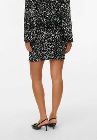 Zwart paillettenjurk met lange mouwen en een aansluitende pasvorm, met een mini-lengte. Draag het met zwarte slingback hakken. Glad huidtinten zichtbaar.