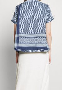 Kortärmad blå skjorta med mönstrad textur och kontrasterande ränder. Lätt material, avslappnad passform och rundad nederkant.