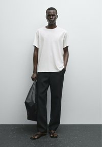 Hvid kortærmet T-shirt, løstsiddende sorte bukser, sort læder tote taske og brune flip-flops. Glat stof og enkelt design.