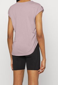 Top corto de manga corta en púrpura con un ajuste relajado y dobladillo redondeado, combinado con pantalones cortos ajustados negros. Textura de tela suave.