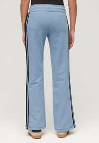 Niebieskie szerokie dresy o miękkiej teksturze, z czarnymi paskami po bokach i ściągaczem w talii. Lekki, casualowy krój odpowiedni na czas wolny.