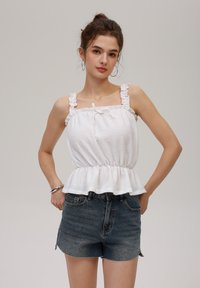 Hvit peplum-top med volangstriper og snøring, kombinert med høy midje mørke denimshorts. Glatt tekstur, uformell design.