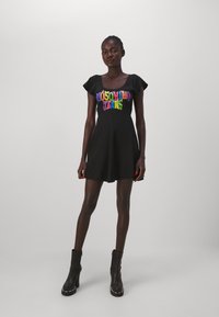 Fekete korcsolyás ruha rövid, fodros ujjakkal és színes "Moschino Jeans" logóval a mellkason. A modellen fekete magassarkú csizma van.