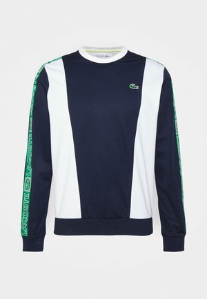 Donkerblauwe en witte sporttrui met lange mouwen, groene Lacoste-branding op de mouwen en een groen krokodillenlogo op de linkerborst.