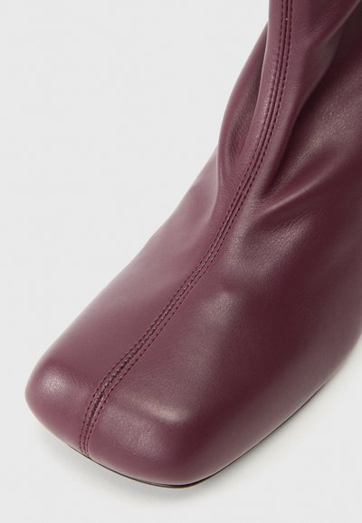 Bottine en cuir bordeaux avec un bout carré, présentant une texture lisse et des coutures visibles le long de la couture avant.