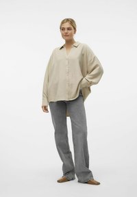 Camicia beige con colletto, vestibilità ampia, tessuto texturizzato; abbinata a jeans grigi a zampa d'elefante e scarpe slip-on marroni.