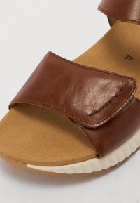 Sandale en cuir brun avec deux sangles ajustables, semelle intérieure beige moulée et semelle de couleur claire, présentant des coutures et une texture visibles.