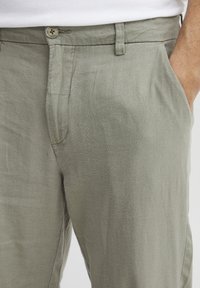 Light green linen trousers featuring a button closure, side pockets, and a textured fabric with a relaxed fit.