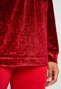 Haut en velours rouge avec un motif géométrique texturé, manches longues et ourlet côtelé, assorti à un legging rouge ajusté.
