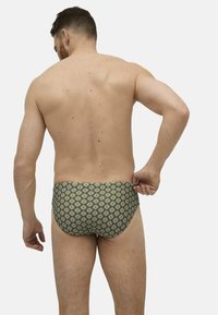 Bañador verde con estampado que presenta un diseño geométrico con acentos rojos y blancos. El material parece suave y tiene una forma ajustada.