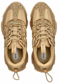 Zapatillas beige con parte superior de malla y acentos de cristal, que presentan superposiciones texturizadas y un lazo en el talón para facilitar su uso.