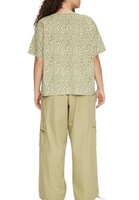 Olive green blouse with white polka dots, short sleeves, and a loose fit, paired with light beige cargo pants featuring side pockets.