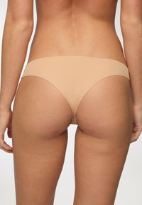 Tanga beige senza cuciture realizzata in materiale morbido ed elastico. Presenta un design minimalista con una vita bassa e bordi lisci.