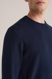 Mornarska pulover s krojem okroglega izreza iz mehkega, strukturiranega materiala; oprijet kroj z minimalnimi šivi, kar poudarja čistem, klasičnem dizajnu.