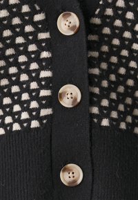 Μαύρο κασκόλ με πλεκτό γεωμετρικό μοτίβο σε μπεζ, με τέσσερις στρογγυλούς, διακοσμημένους κουμπιά κατά μήκος του μπροστινού μέρους. Μαλακή υφή.