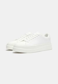 Sneakers bianchi con una texture liscia, punta rotonda, suola piatta e accenti testurizzati. Presentano un design con lacci e uno stile minimalista.