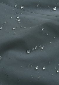 Tissu gris foncé avec une texture lisse, présentant des gouttes d'eau à la surface, indiquant des propriétés résistantes à l'eau.