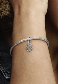 Strieborný pletený náramok s príveskom hamsa s dizajnom oka. Hladký povrch a minimalistický dizajn dôrazne zdôrazňujú detail prívesku.