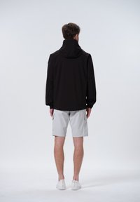 Chaqueta ligera negra con capucha, de textura suave. Combinada con pantalones cortos grises claros. Diseño simple con un mínimo de detalles.