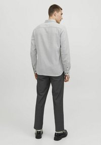 Lichtgrijze button-up shirt met een kraag, lange mouwen en twee knoopmanchetten, gecombineerd met donkergrijze broek en zwarte schoenen.