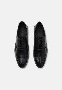 Pantofi de piele negri, cu o textură netedă, vârf rotund și șireturi înguste, având un design elegant și minimalist.